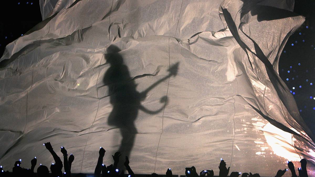 Zum Auftakt der Show zeigt sich Prince hinter einem Vorhang mit einer eigenartig geschwungenen Gitarre