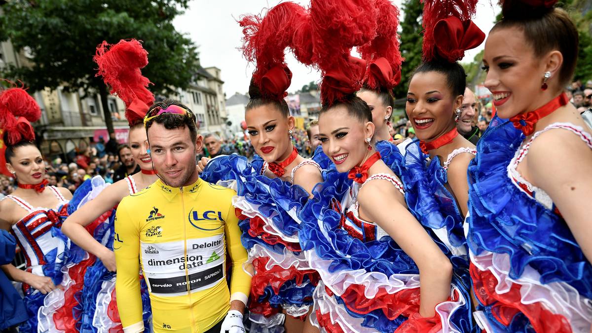 An Tag zwei startet Mark Cavendish erstmals in diesem Jahr im Gelben Trikot. Vor dem Start posiert der Brite mit einigen französischen Tänzerinnen