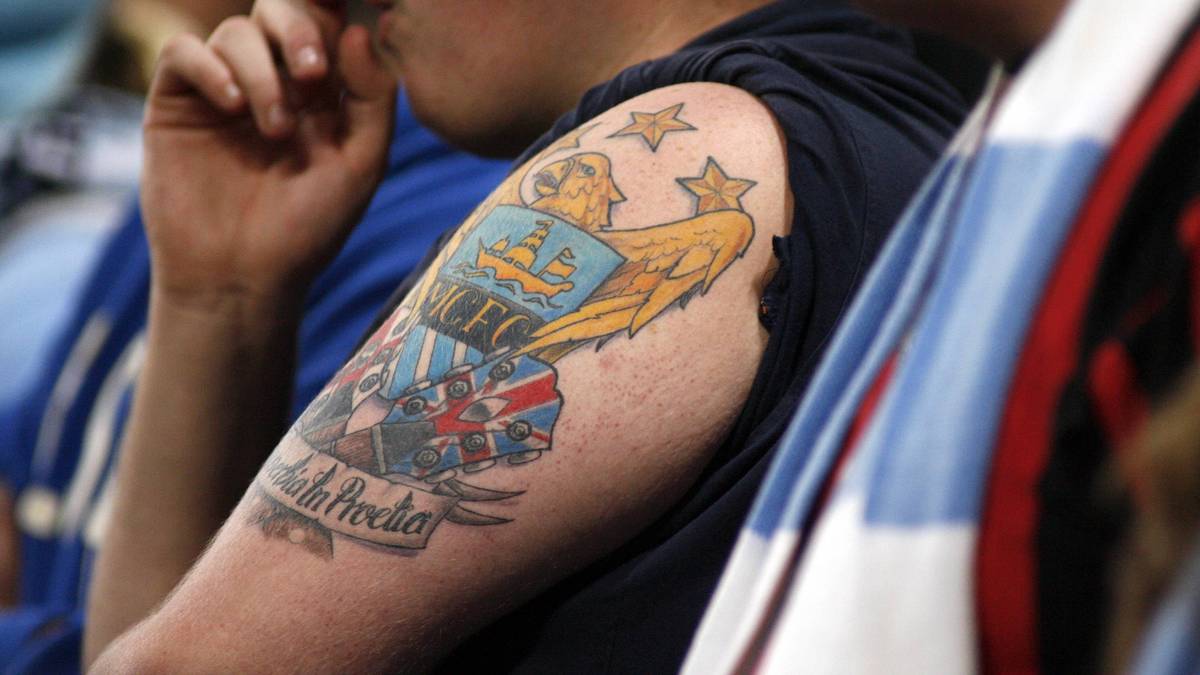 Die Liebe englischer Fußballfans geht weit - sogar so weit, dass Vereinswappen auf Rücken Brust oder anderen Körperteilen der Fans landen. Dieser Fan von Manchester City hat sich das 1997 vom Verein neu gestaltete Logo auf den Oberarm stechen lassen. Am markantesten darauf ist der Adler und der Spruch "Superbia in Proelia" (Stolz im Kampf)