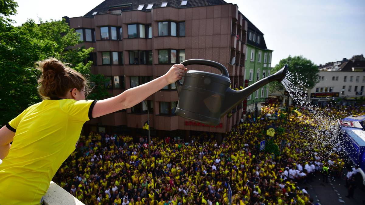 Die Menge muss in der brütenden Hitze auf die Mannschaft warten. Mithilfe einer Gießkanne versucht diese Anhängerin, für Kühlung zu sorgen...