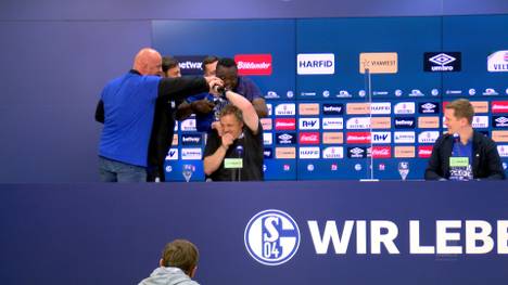 Schalke 04-Trainer Mike Büskens wird auf der Pressekonferenz, nach dem Wiederaufstieg in die Bundesliga, unterbrochen. Er bekommt die Bierdusche von den "Hammerwerfern"