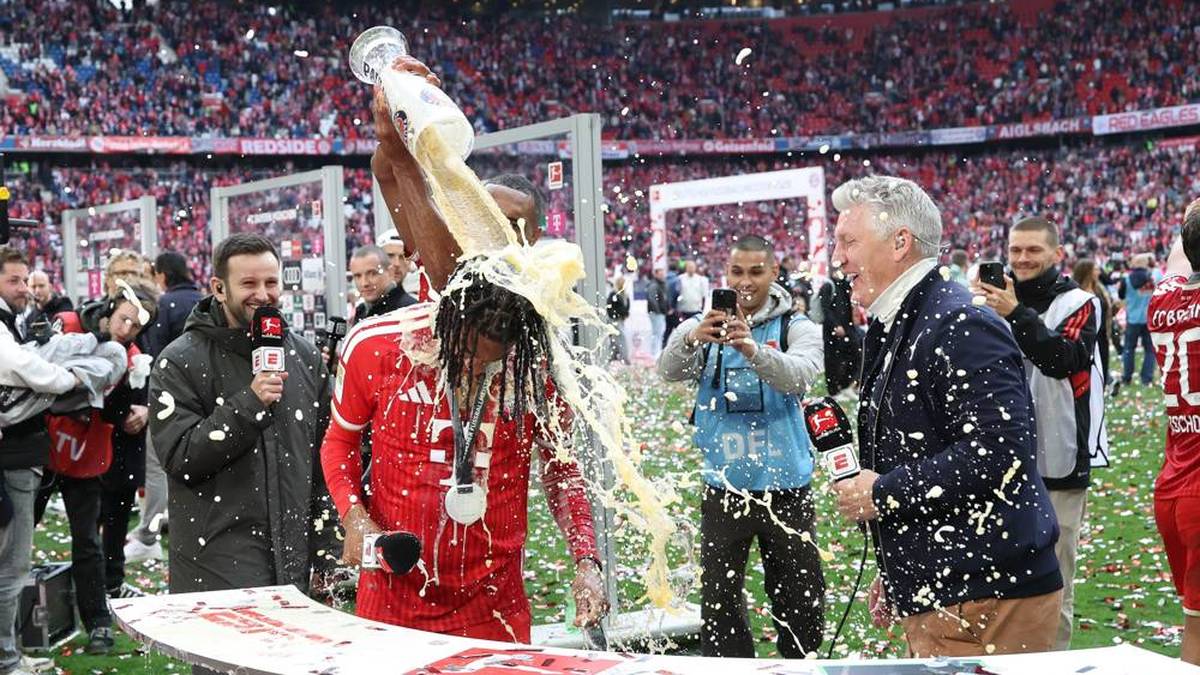 Sein Teamkollege Jonathan Tah schleicht sich von hinten an und kippt dem Franzosen das komplette Glas über den Kopf