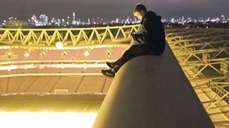 Der junge Kletterer sitzt auf dem Dach des Emirates Stadium