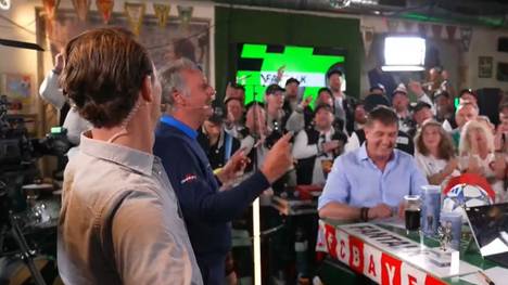 Die SPORT1-Experten Thomas Strunz und Peter Neururer werden im Fantalk von einem Männerchor empfangen.