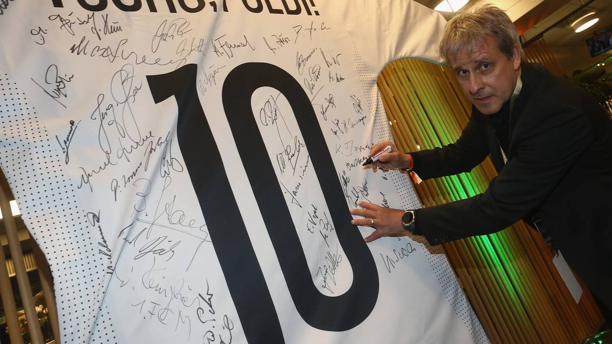 Im Stadion unterschreiben ehemalige Nationalspieler auf einem überdimensionalen Trikot. Hier Pierre Littbarski - einer der Vorgänger Podolskis als Publikumsliebling des 1. FC Köln