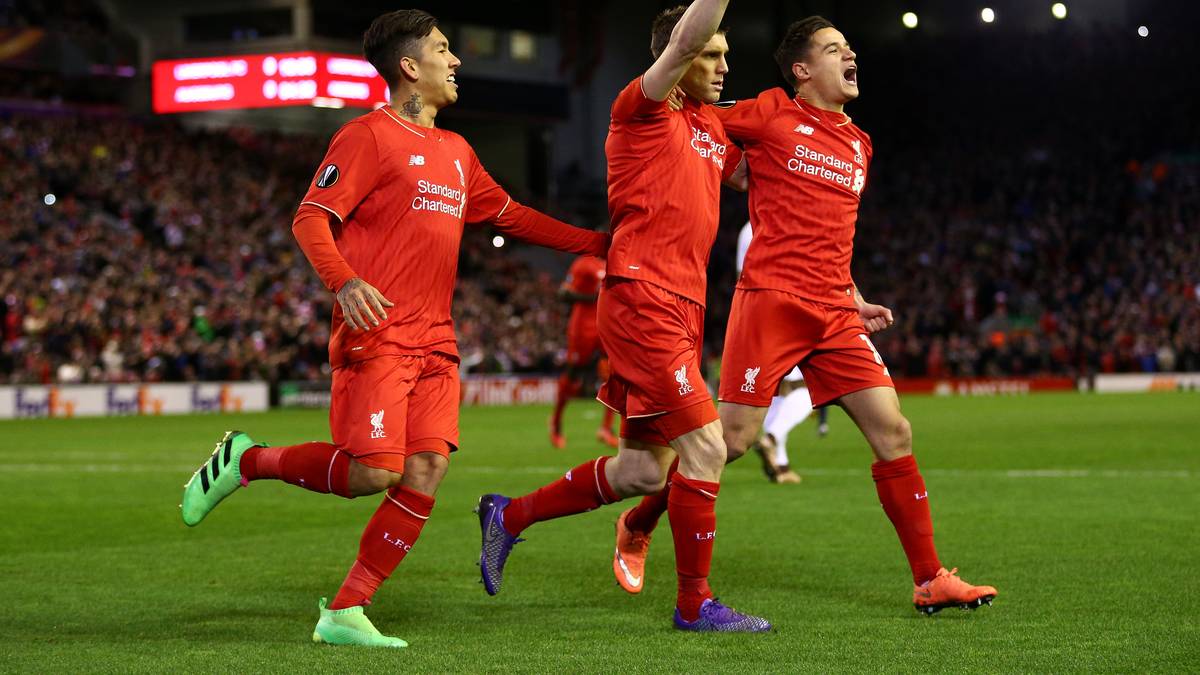 Milner (M.) streckt den Zeigefinger in die Luft. Seine Teamkollegen Roberto Firmino und Philippe Coutinho umringen ihn