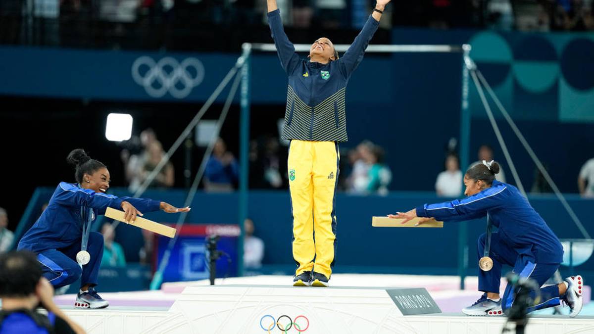 Simone Biles und Jordan Chiles (r.) ehren die Brasilianerin Rebeca Andrade bei der Medaillenzeremonie nach dem Finale im Bodenturnen der Frauen