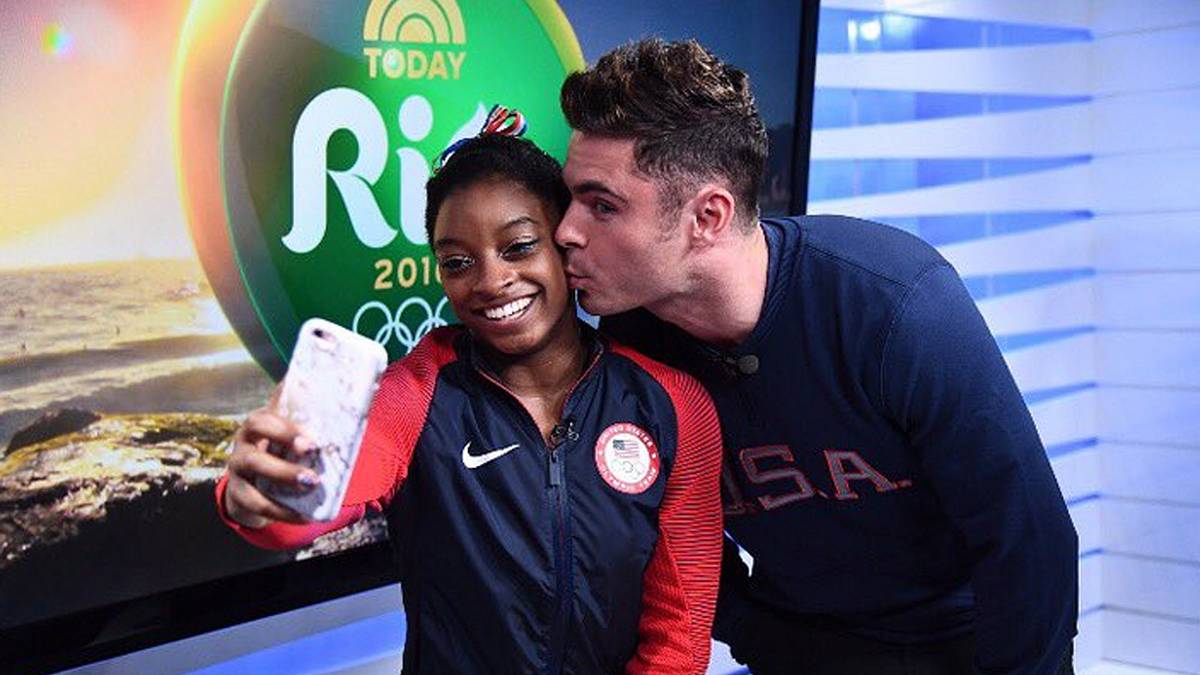 Turn-Superstar Simone Biles (l.) kommt aus dem Strahlen nicht mehr heraus, als Schauspieler und Teenie-Schwarm Zac Efron sie bei Olympia besucht und ihr ein Küsschen aufdrückt