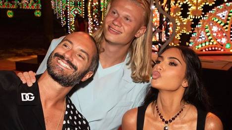Kim Kardashian und Erling Haaland posieren auf dem Event von Dolce & Gabbana für ein Foto, zum Leidwesen der City-Fans. Die fürchten nun einen "Fluch", der wohl auf Kardashian liege soll.