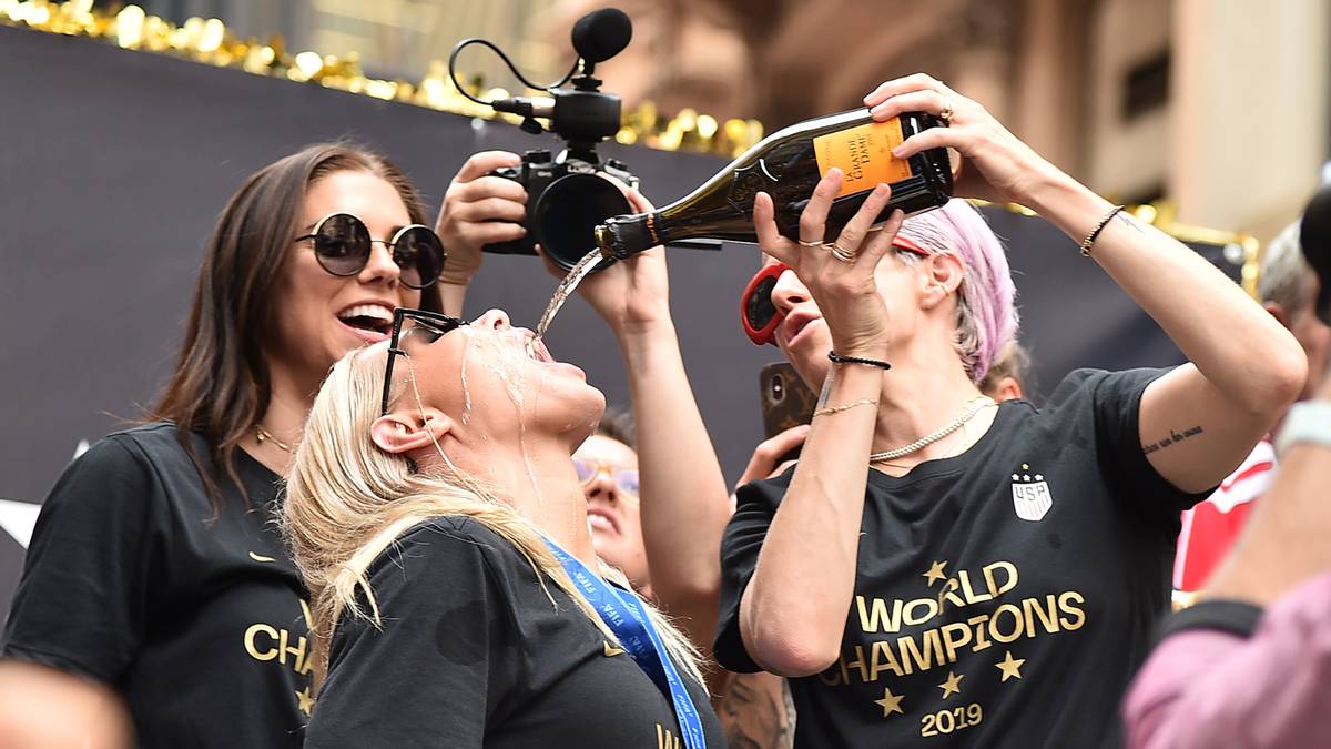 Auf dem Umzugswagen geht es feucht-fröhlich zu. Rapinoe verteilt als fürsorgliche Kapitänin Schampus an die Mitspielerinnen