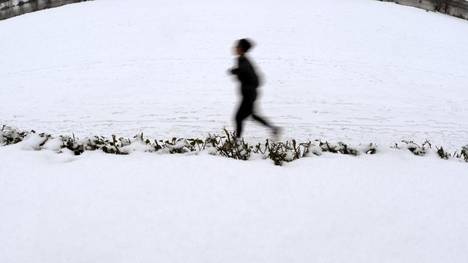 Eine Joggerin läuft an der mit Schnee bedeckten Neckarpromenade in Heidelberg entlang