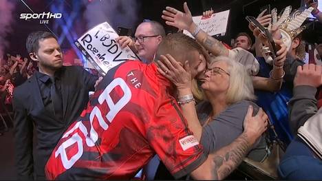 Nathan Aspinall gibt bei seinem Walk-On der Frau von Gegner Andrew Gilding einen Kuss. SPORT1 klärt auf, weshalb Evelyn Gilding so herzlich von Aspinall behandelt wird.