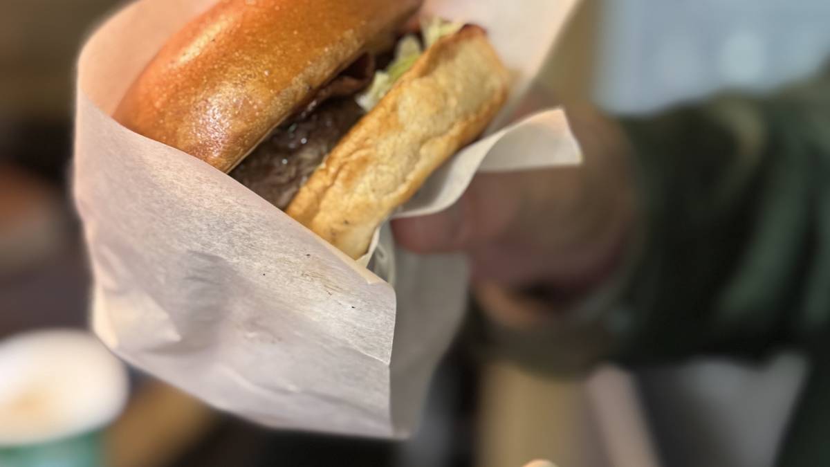 Der Burger wird in einem Brioche Bun mit Gewürzgurken, einer Burgersauce, Eisbergsalat und amerikanischem Käse serviert. 