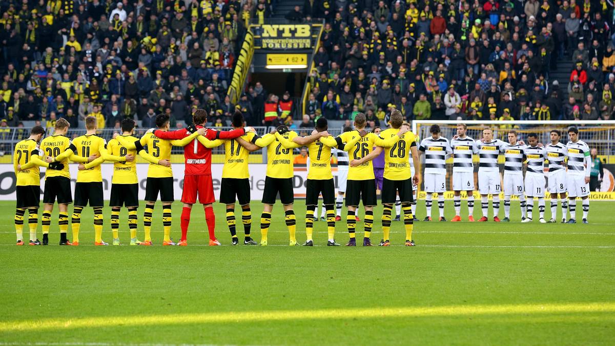 Genau wie in Dortmund. Gladbach- und BVB-Spieler reihen sich am Mittelkreis auf und gedenken der Opfer