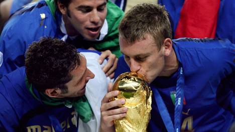 Berlin, GERMANY:  Italian defender Marco Materazzi (L) looks on as Italian midfielder Daniele De Rossi (R) kisses the World Cup trophy following their victory in the World Cup 2006 final football match between Italy and France at Berlin's Olympic Stadium, 09 July 2006.  Italy won 5-4 in the penalty shootout after the teams finished in extra time 1-1.     AFP PHOTO / ODD ANDERSEN  (Photo credit should read ODD ANDERSEN/AFP via Getty Images)