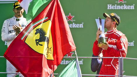Sebastian Vettel mit Pokal und Ferrari-Fahne vor Lewis Hamilton