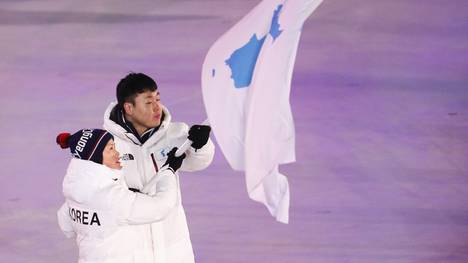 Eine südkoreanischer Bobfahrer und eine südkoreanische Eishockeyspielerin laufen  gemeinsam ein