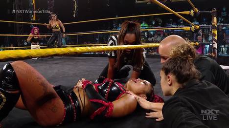 Xia Li liegt bei WWE NXT verletzt am Boden, während Champion Raquel Gonzalez und Dakota Kai im Hintergrund warten