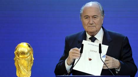 Sepp Blatter hält den Ausrichter der WM 2022, Katar, neben dem WM-Pokal in der Hand