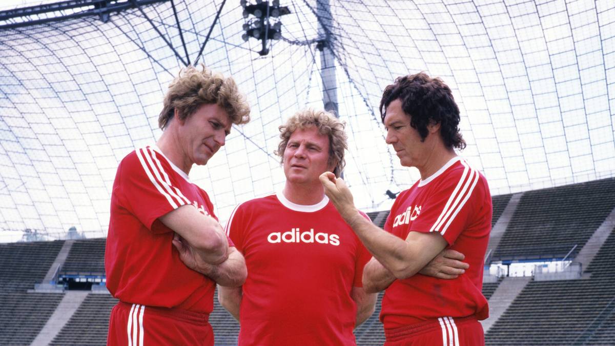 Ältere Herrschaften mit jungen Perücken: Karl-Heinz Rummenigge, Uli Hoeneß und Beckenbauer im Siebziger-Look im Olympiastadion