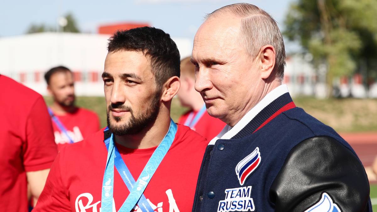 Stilecht im "Team Russia"-Sakko mit russischer Flagge auf dem Ärmel beglückwünscht Putin die Teilnehmer zu ihren herausragenden Leistungen