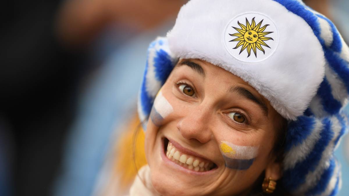 Breit in die Kamera grinst auch diese Dame. Sie trägt eine Uschanka, eine russische Wintermütze, in den Farben von Uruguay