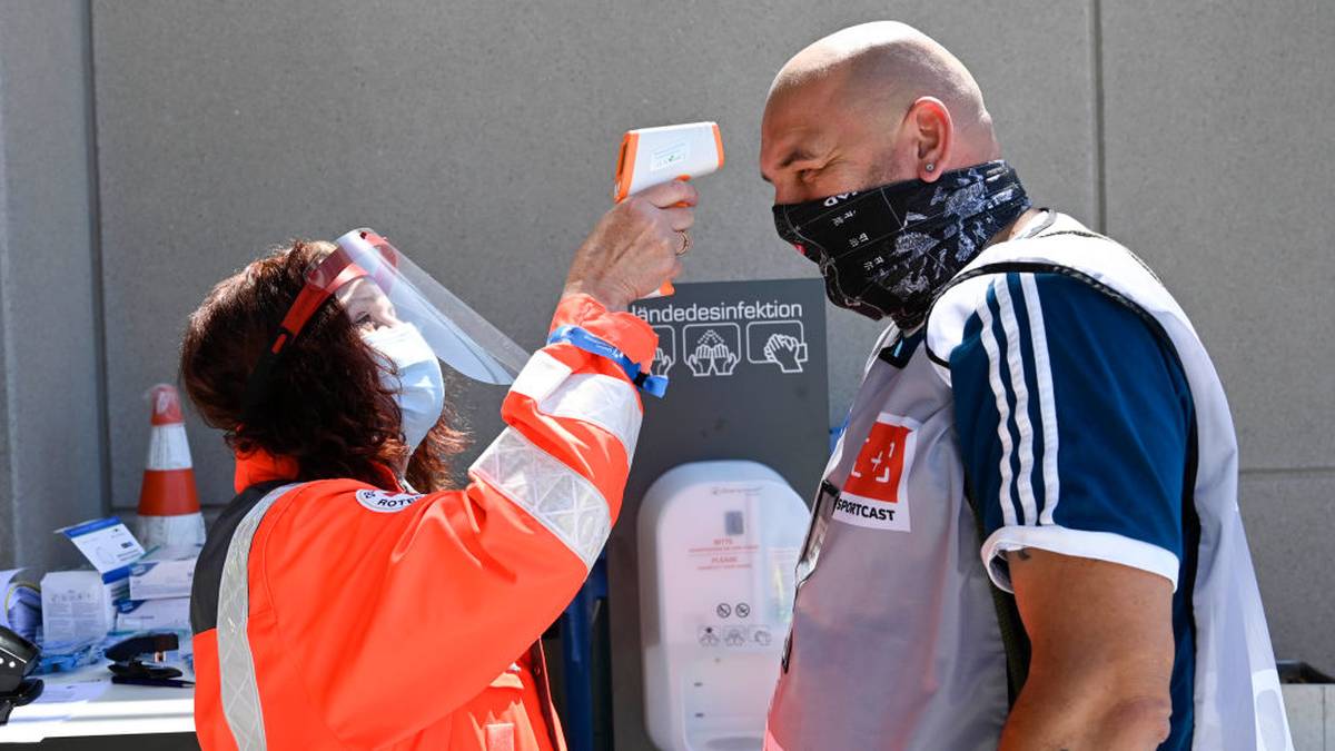 SINSHEIM, GERMANY - MAY 16: A member of the Red Cross measures the temperature of photographer Torsten Wagner at the entrance of the stadium prior to the Bundesliga match between TSG 1899 Hoffenheim and Hertha BSC at PreZero-Arena on May 16, 2020 in Sinsheim, Germany. The Bundesliga and Second Bundesliga is the first professional league to resume the season after the nationwide lockdown due to the ongoing Coronavirus (COVID-19) pandemic. All matches until the end of the season will be played behind closed doors. (Photo by Thomas Kienzle/Pool via Getty Images)