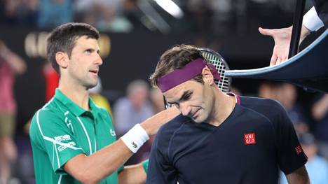 Serbia's Novak Djokovic (L) prepares to shake hands with the umpire as Switzerland's Roger Federer walks off the court after their men's singles semi-final match on day eleven of the Australian Open tennis tournament in Melbourne on January 30, 2020. (Photo by DAVID GRAY / AFP) / IMAGE RESTRICTED TO EDITORIAL USE - STRICTLY NO COMMERCIAL USE (Photo by DAVID GRAY/AFP via Getty Images)
