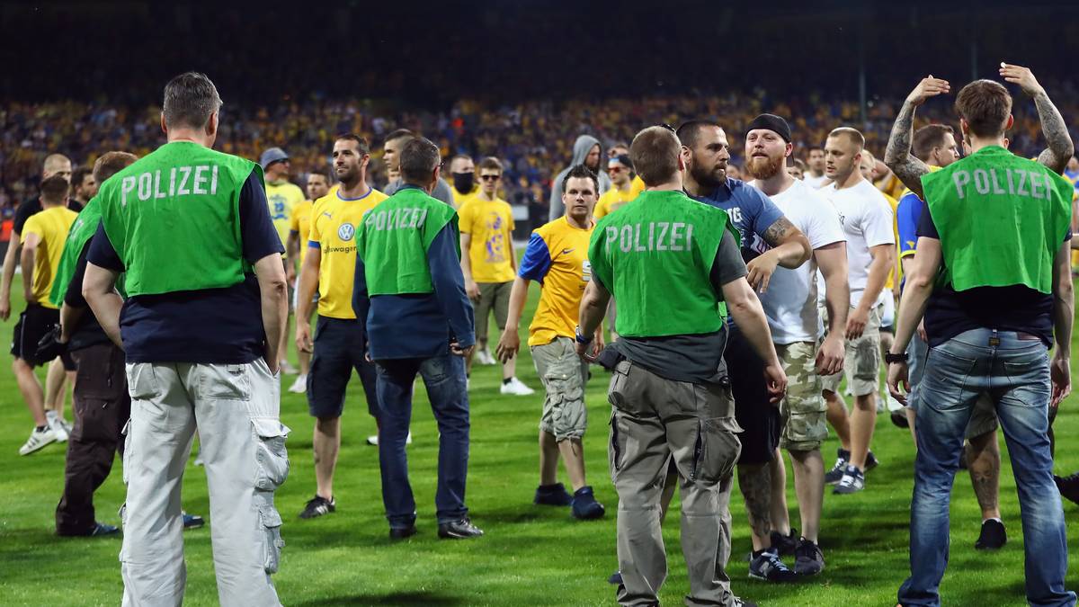 Einige Anhänger stürmen den Rasen des Stadions und marschieren in Richtung Gästekurve. Die Polizei ist sofort mit einem Großaufgebot auf dem Feld und verhindert den Vormarsch der Anhänger. Dennoch fliegt auch noch Pyro-Material in Richtung der Ordnungshüter