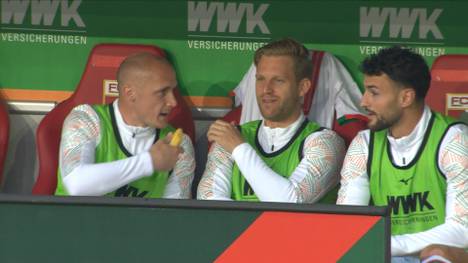 Vor dem Spiel des FC Augsburg gegen den VfB Stuttgart interviewt Sven Michel seine Teamkollegen auf der Auswechselbank mit einer Banane.