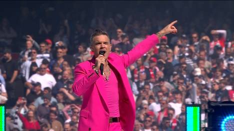 Beim Rugby AFL Grand Final sorgt ein Star-Gast für gute Stimmung. Der komplett in rosa gekleidete Robbie Williams heizt mit einem Medley der Rugby-Meute an.